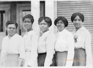 Five African American women stand in a line, facing the camera, in the early 1900s.