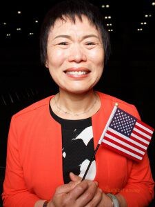 A Chinese woman holds a small American flag while crying happy tears.