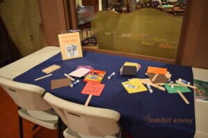 Colorful pieces of construction paper are attached to popsicle sticks and strewn about a table. One paper says 