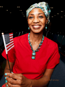 An African woman wears an American flag pin and smiles towards the camera.