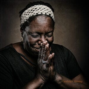 A Black woman looks down with her hands pressed together and touching her face, as if praying.