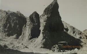 An old car is pictured in front of large rock formations.