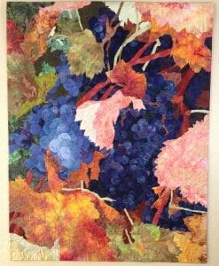 A colorful quilt with green, orange, and pink leaves and purple grapes.